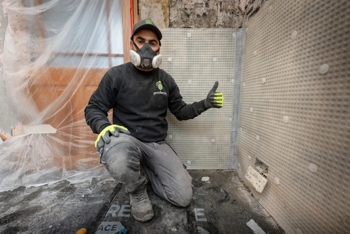Proofterior technician kneeling in front of a freshly installed damp-proof tanking membrane in a period property